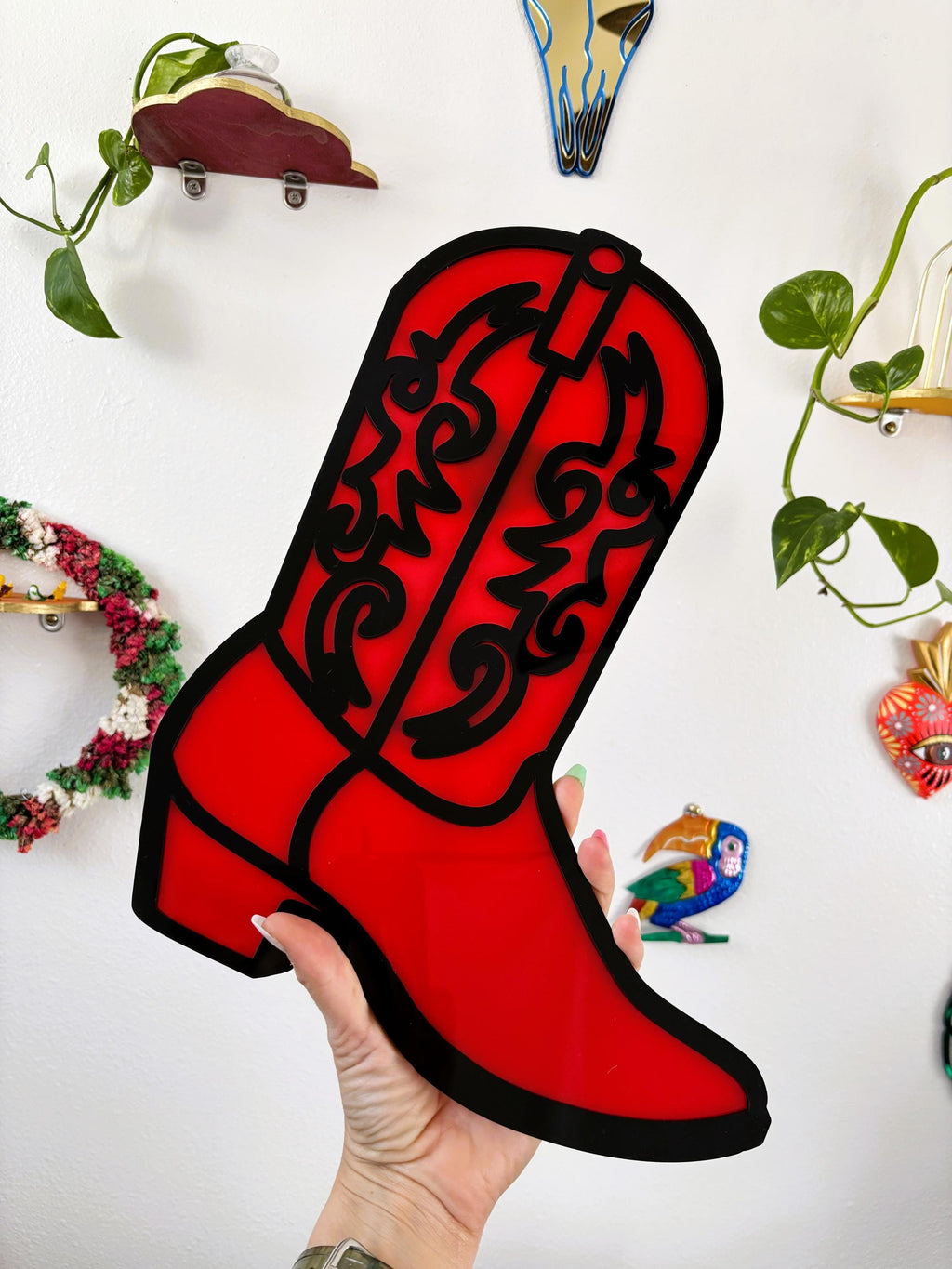 Red cowboy boot-shaped object held by a hand against a white background with decorative elements.