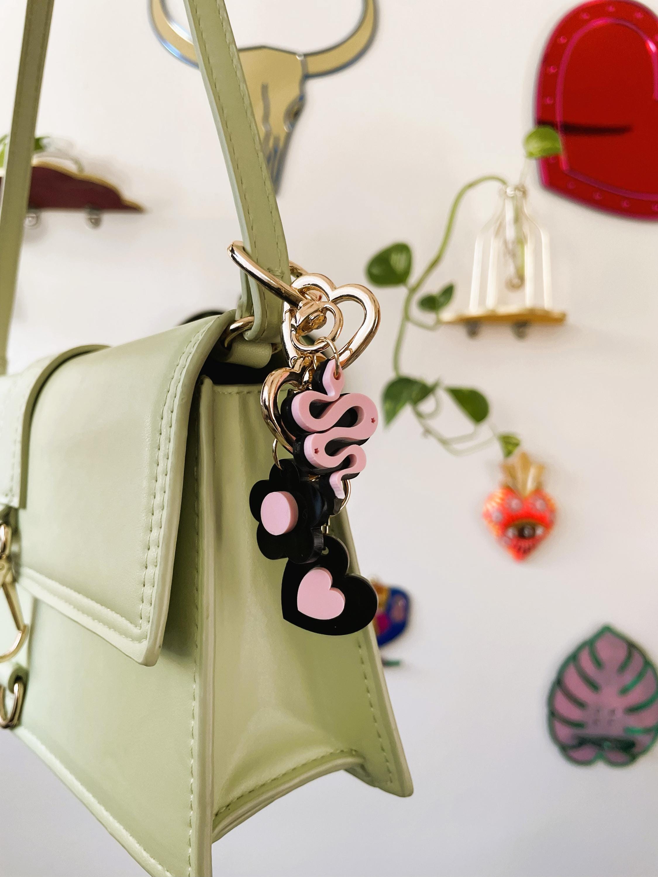 Green handbag with a colorful keychain against a decorative wall.