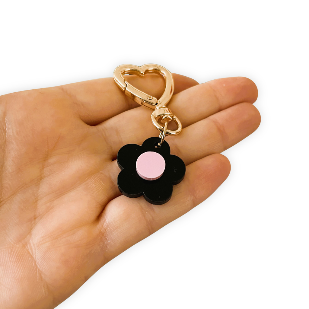 Black flower-shaped keychain with a pink center held in a hand on a white background