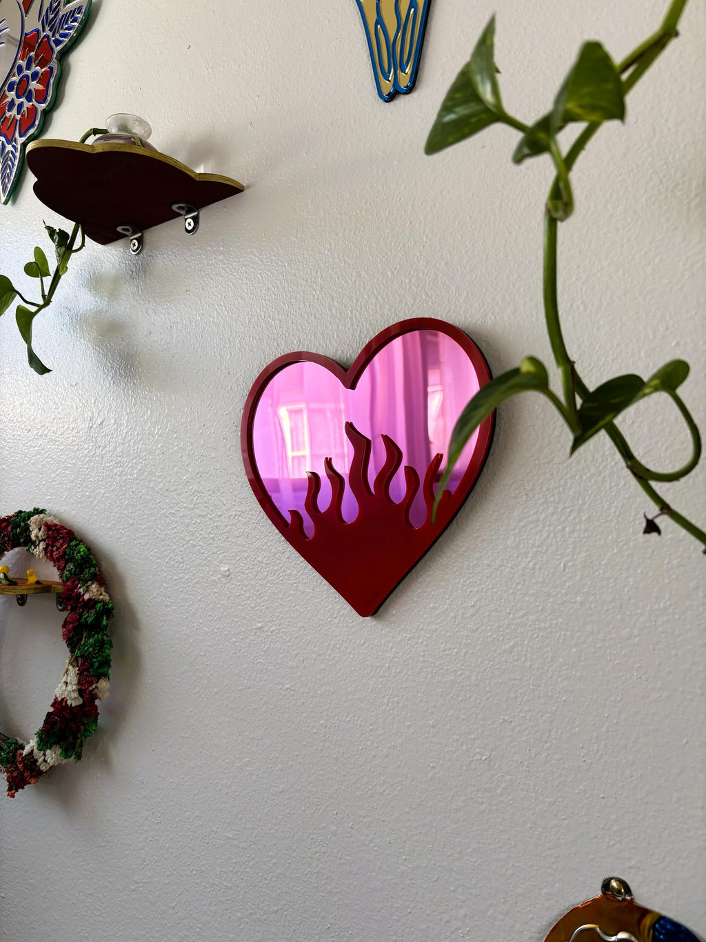 Heart-shaped mirror with pink interior on a white wall with decorative elements.