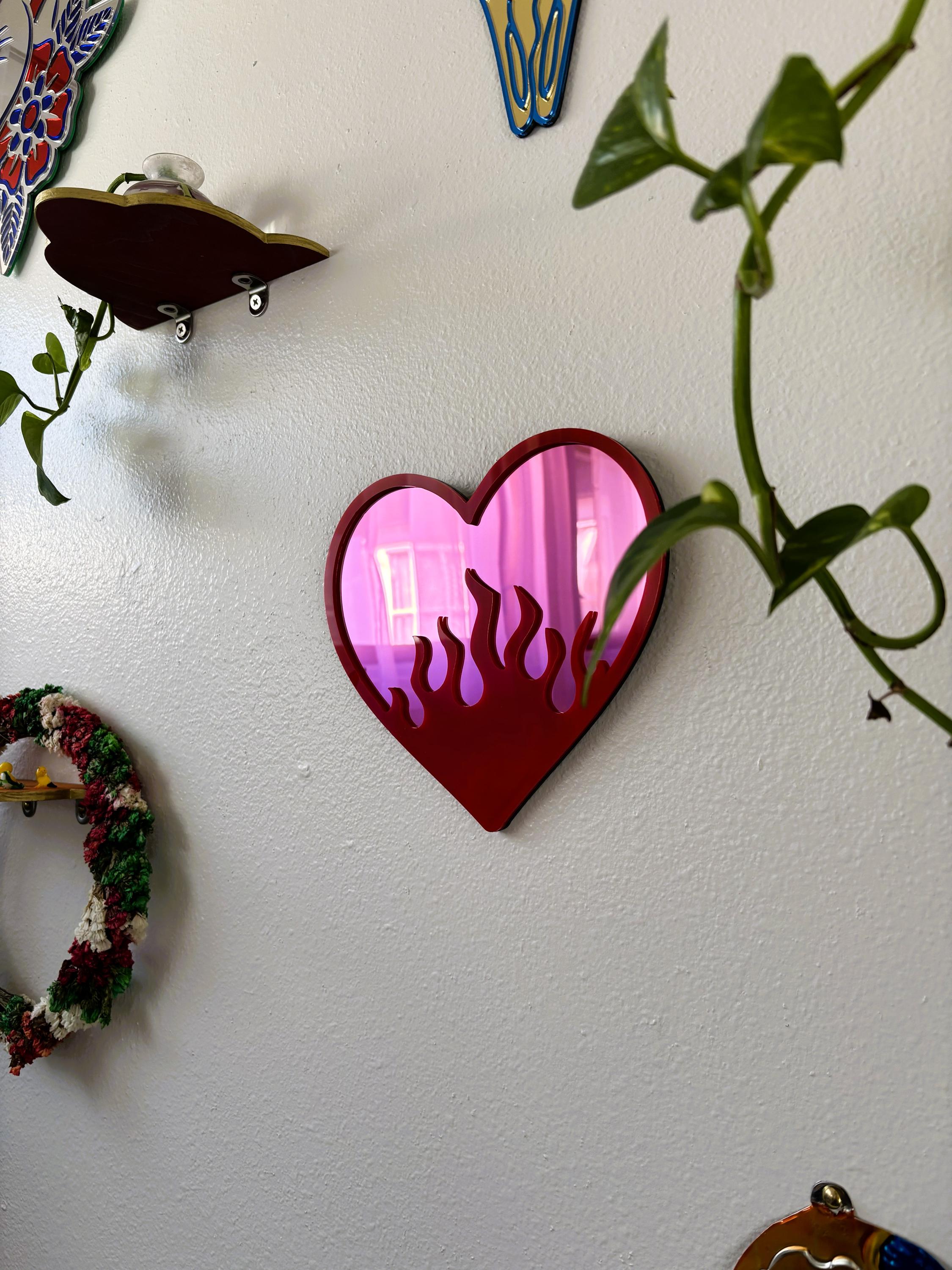Heart-shaped mirror with pink interior on a white wall with decorative elements.
