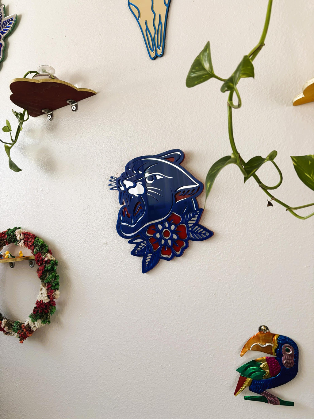 Decorative wall art pieces including a blue panther head, colorful wreath, and bird on a white background with green vines.