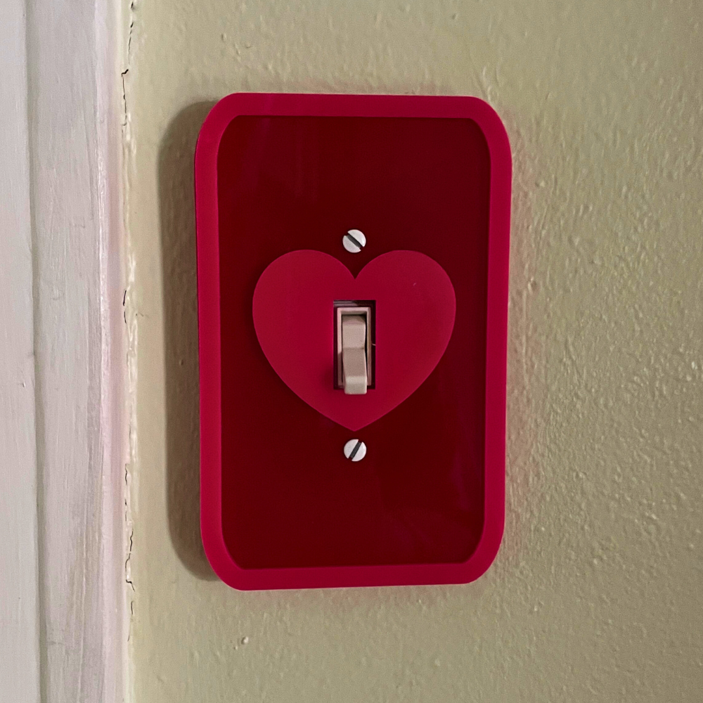 Red light switch cover with a heart design on a beige wall.