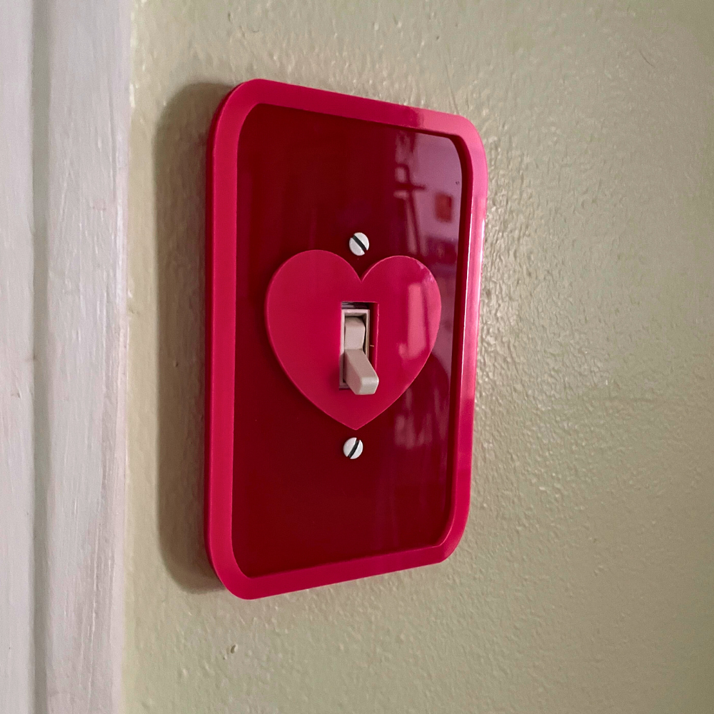Red light switch cover with a heart design on a beige wall.