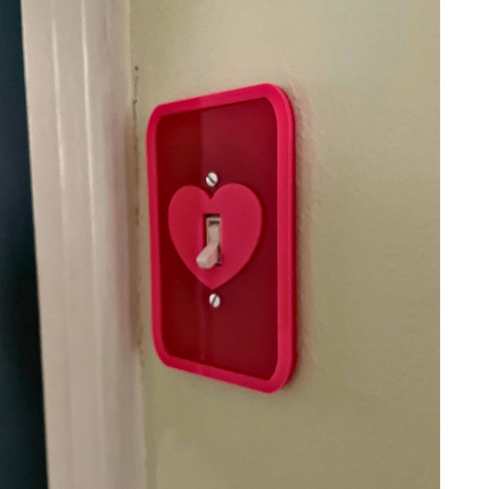 Red light switch cover with a heart-shaped design on a beige wall.