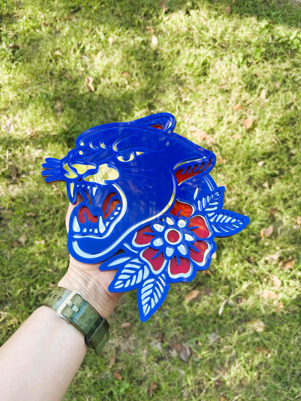 Blue tiger head design with floral elements held by a person against a grassy background