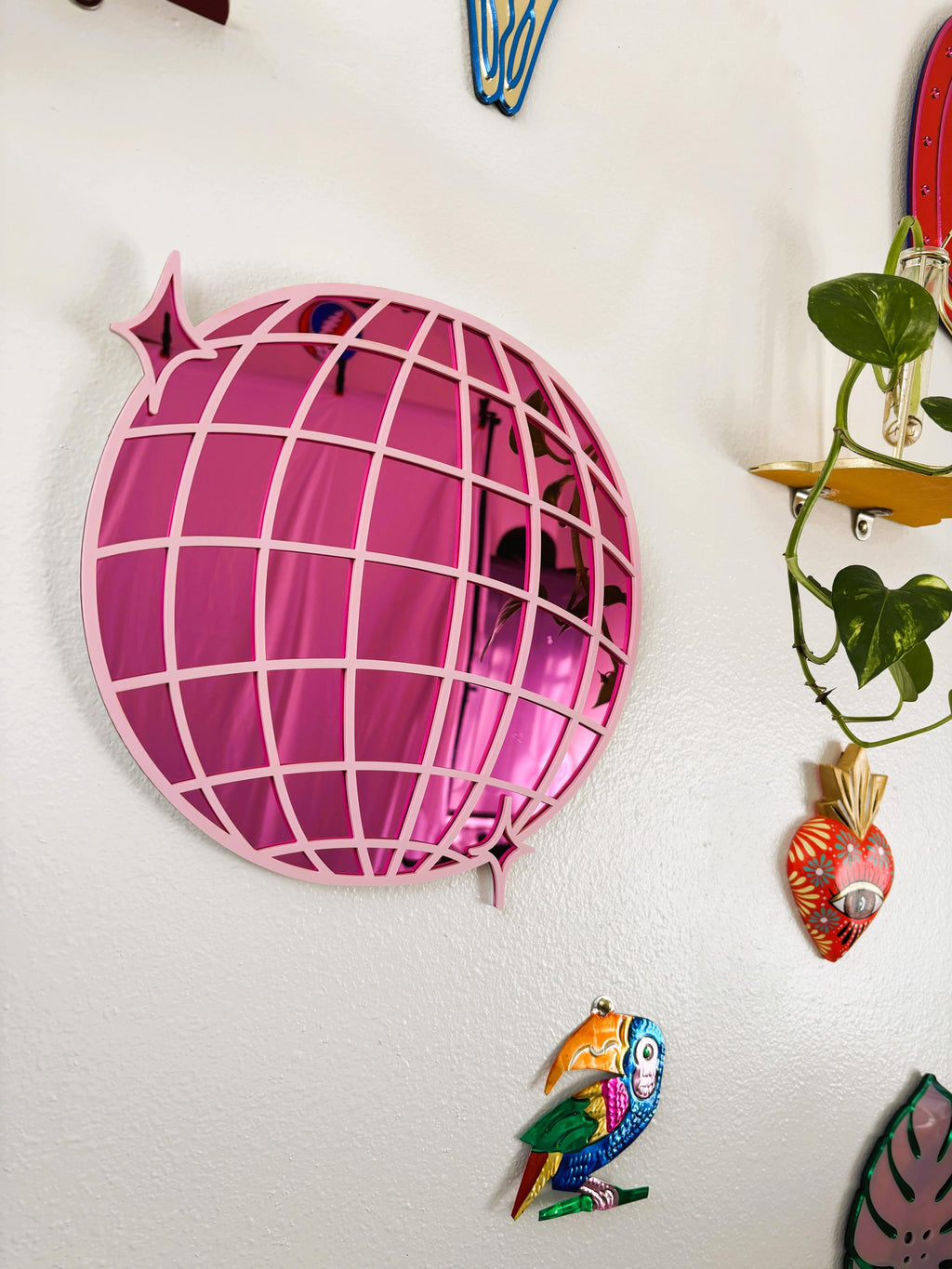 Decorative wall art including a pink fish-shaped mirror and colorful fish figurine on a white wall.
