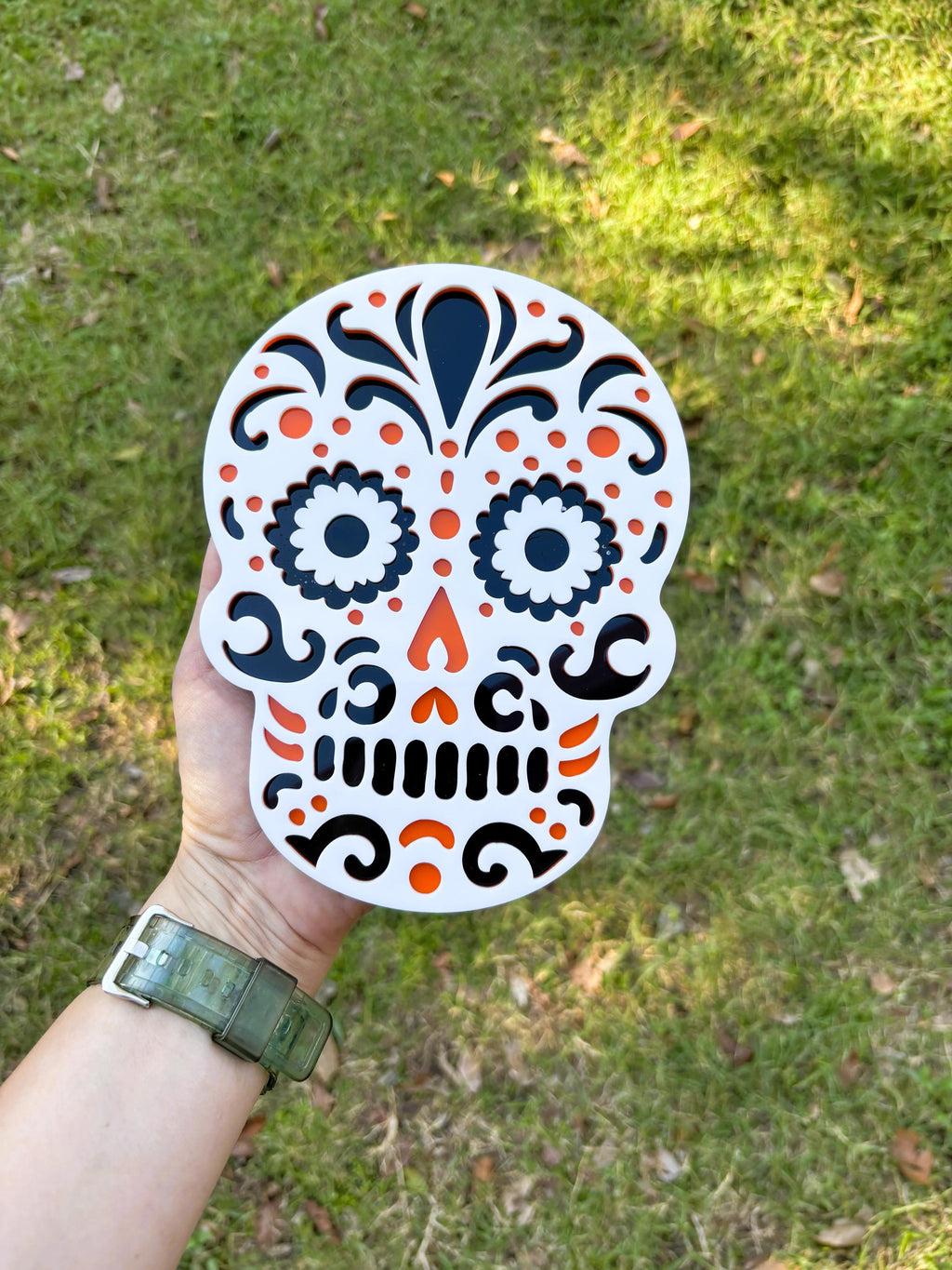 Hand holding a colorful skull-shaped sticker against a grassy background