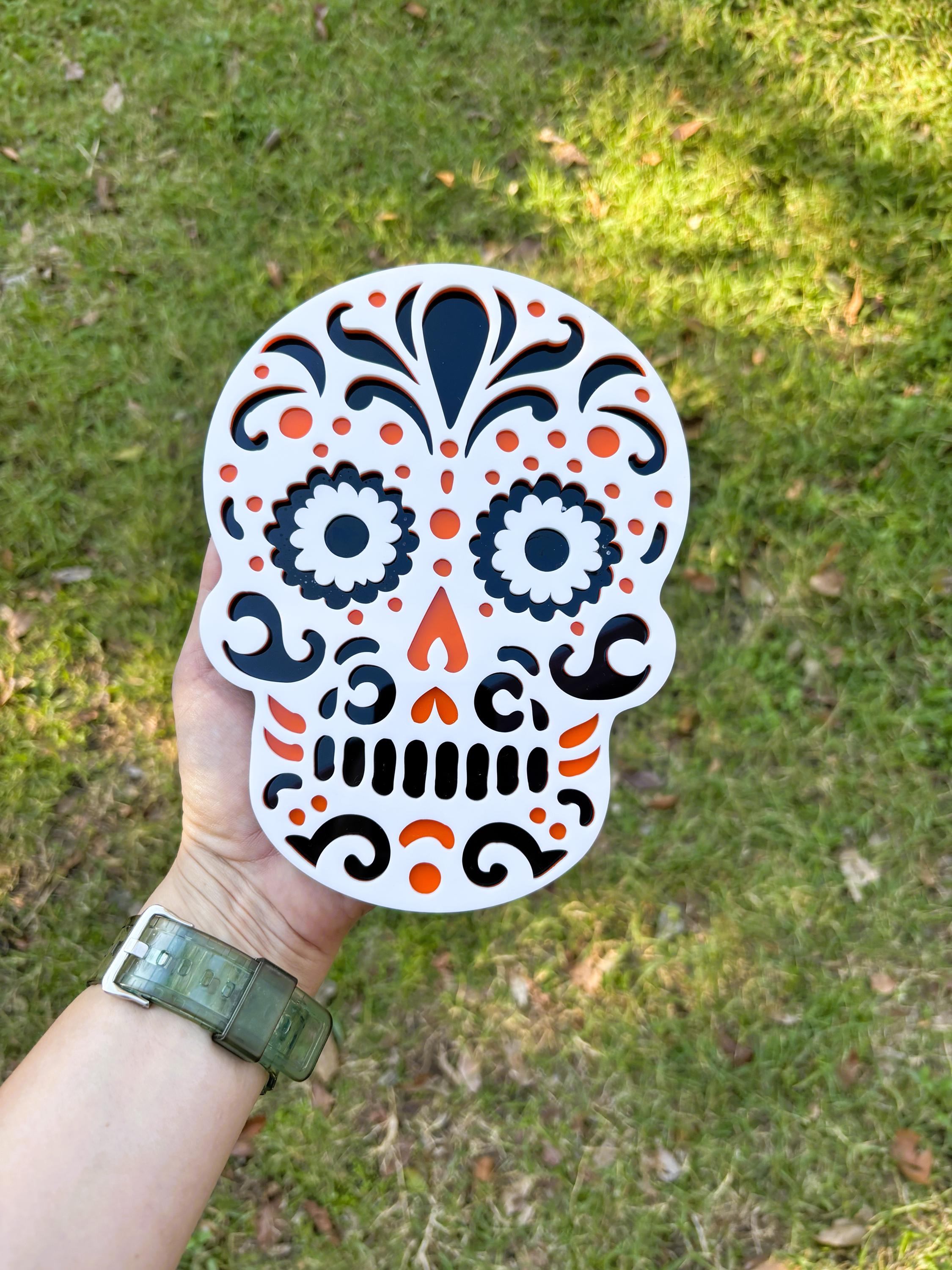 Hand holding a colorful skull-shaped sticker against a grassy background