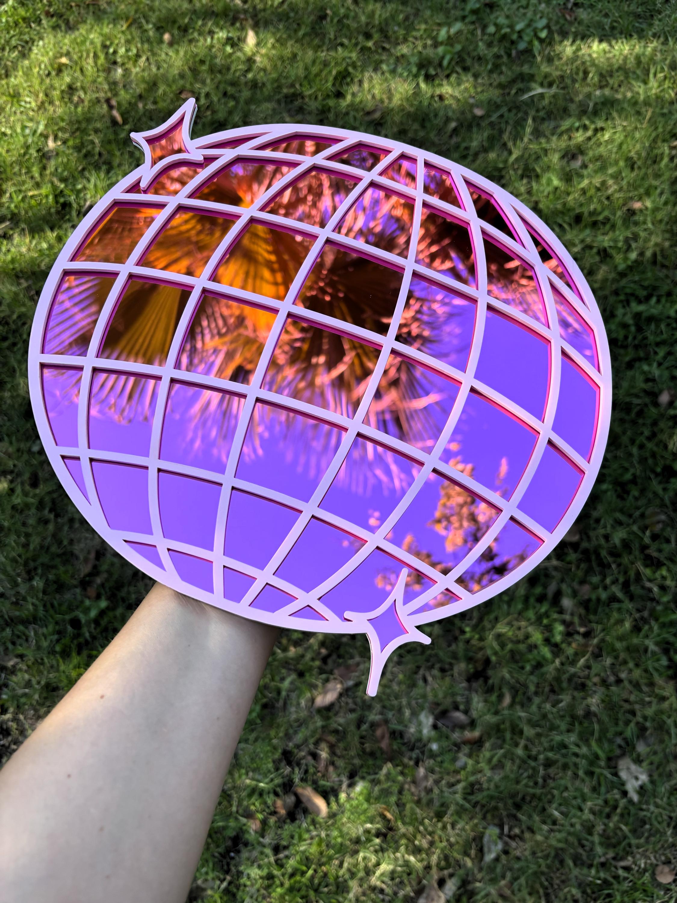 Decorative purple and orange spherical object held by a hand on grass