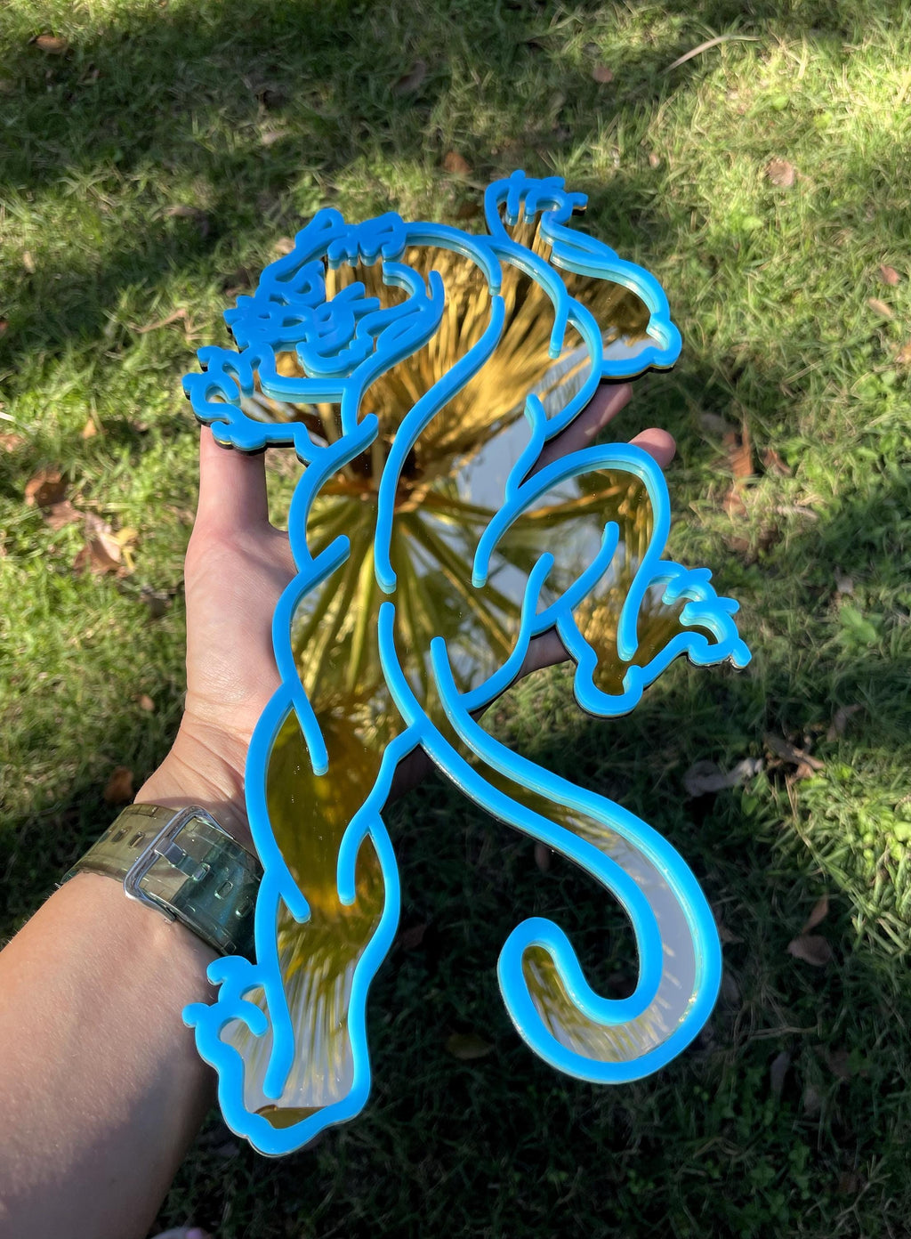 Blue metal dragon sculpture held by a person against a grassy background