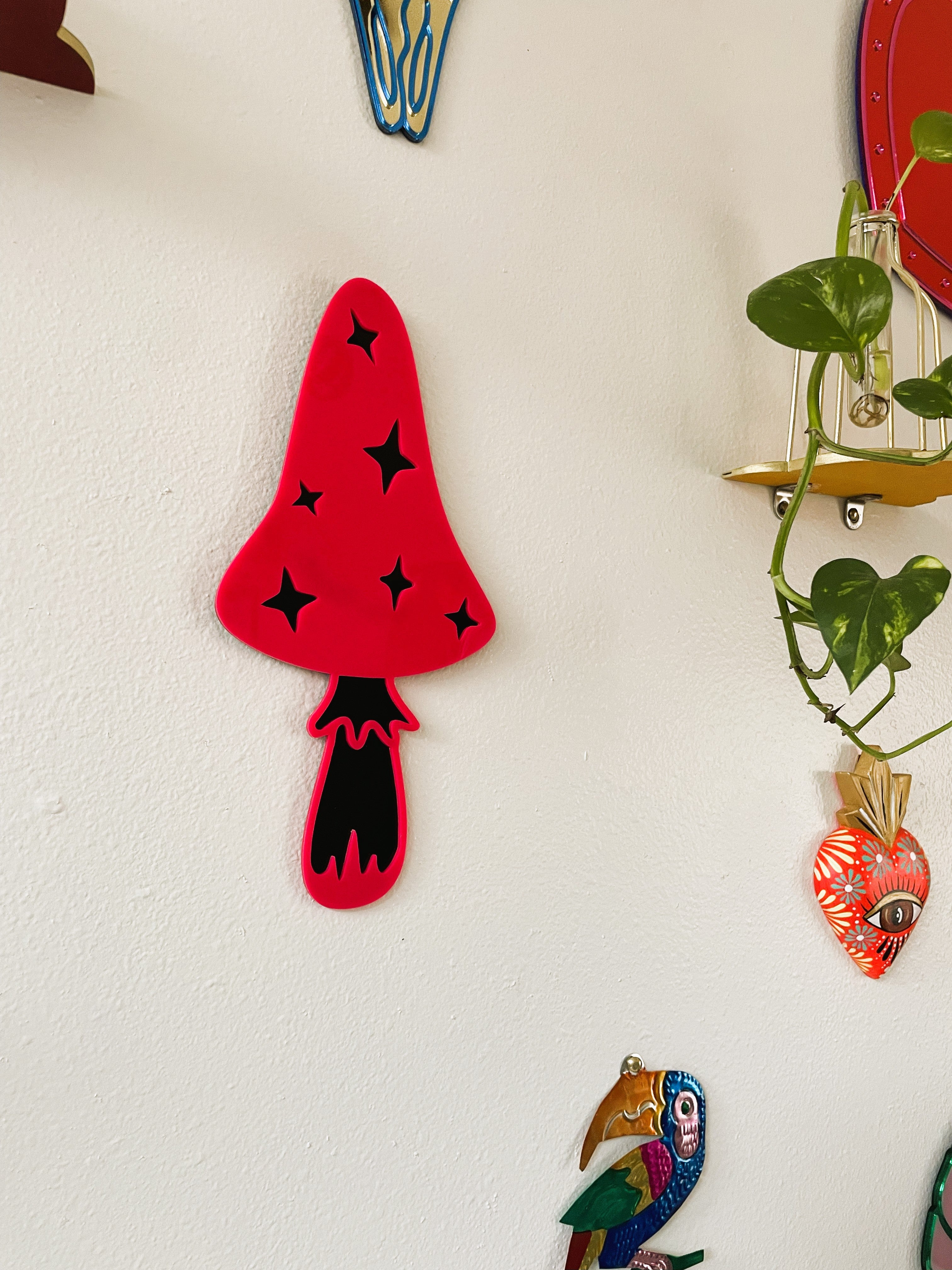 Decorative wall art including a red mushroom with black spots, a parrot, and a plant on a white wall.