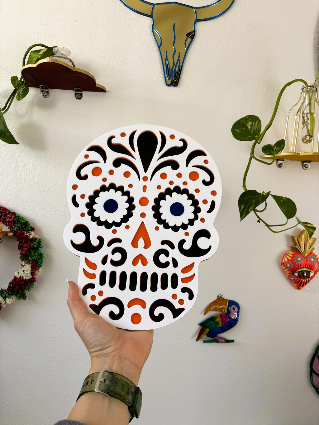 Hand holding a decorative skull with intricate patterns against a wall with various decorations.