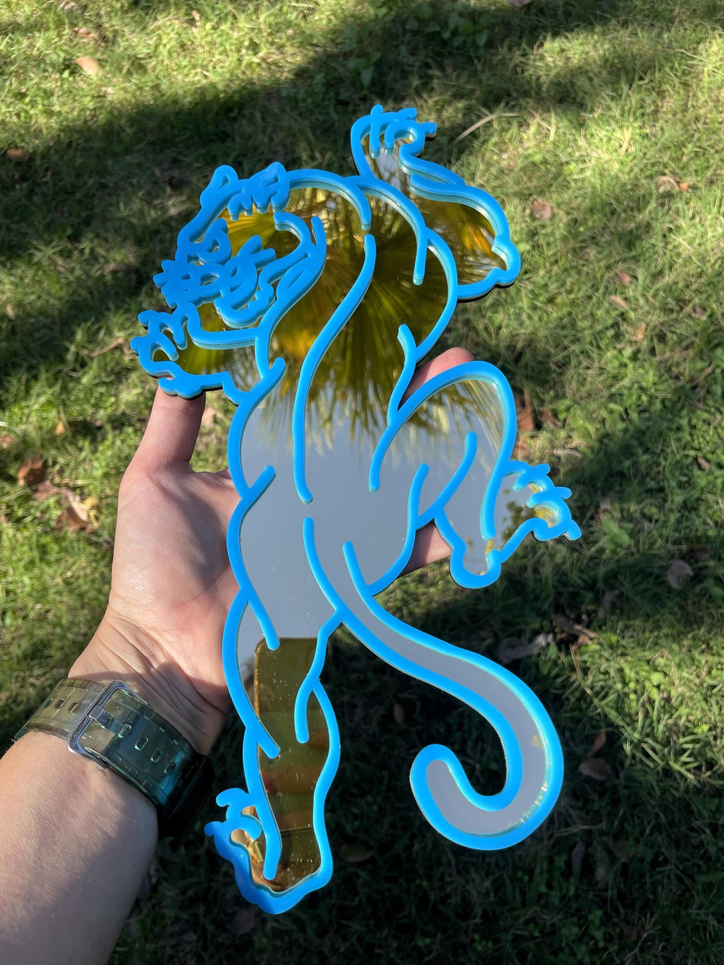 Hand holding a blue and gray seahorse-shaped object against a grassy background