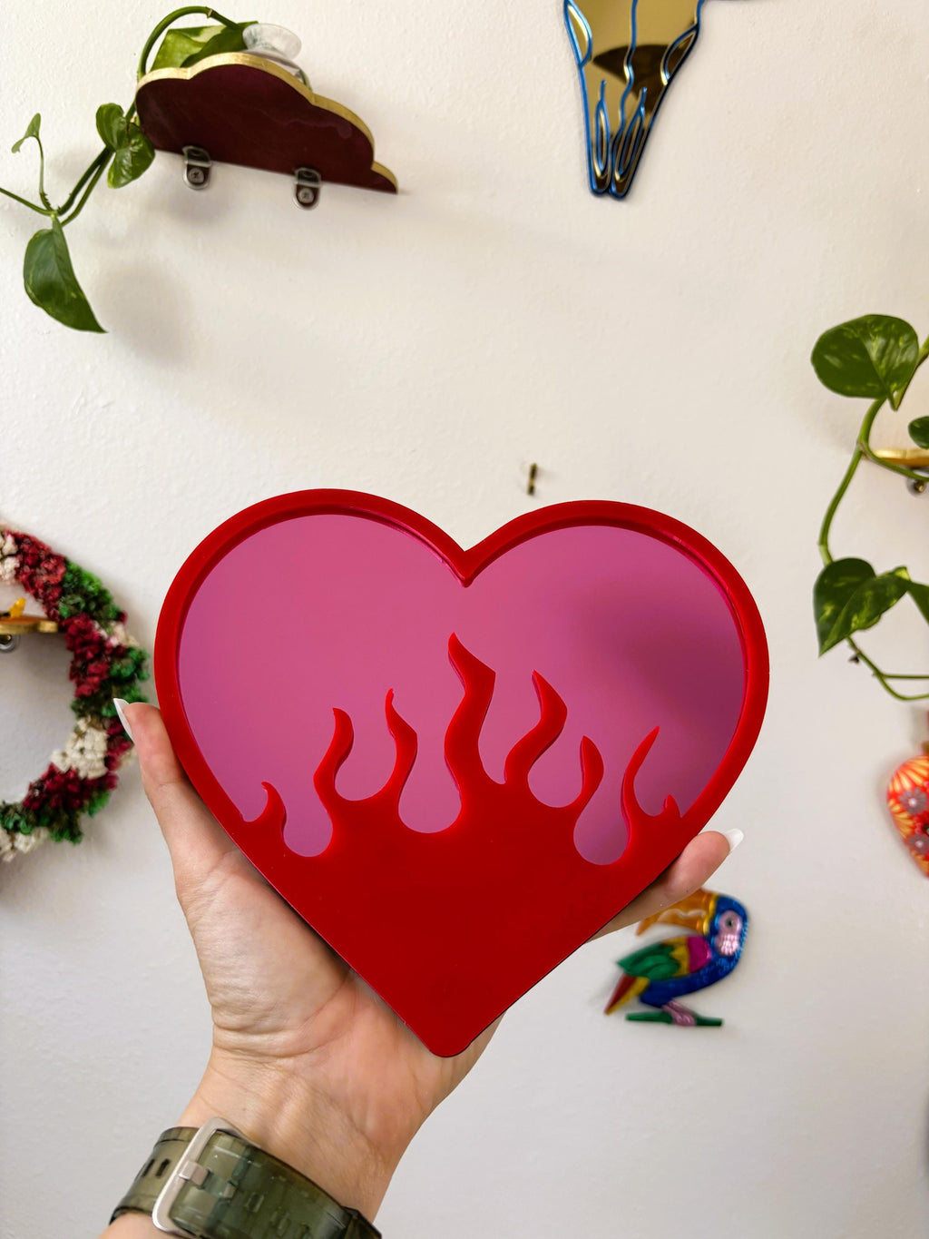 Heart-shaped object with flame design held by a hand against a white background with decorative items.