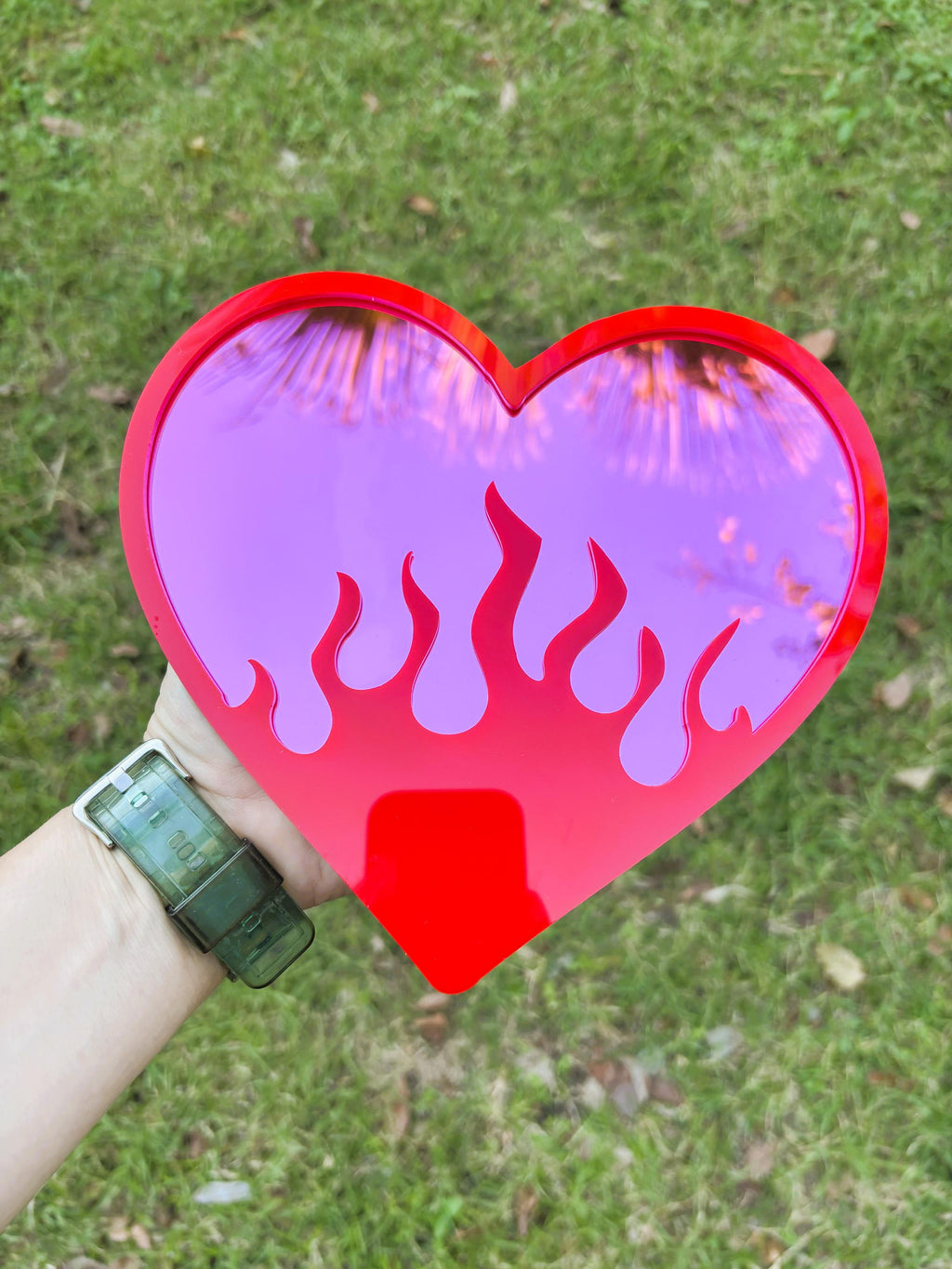 Heart-shaped object with purple flame design held by a person against a grassy background
