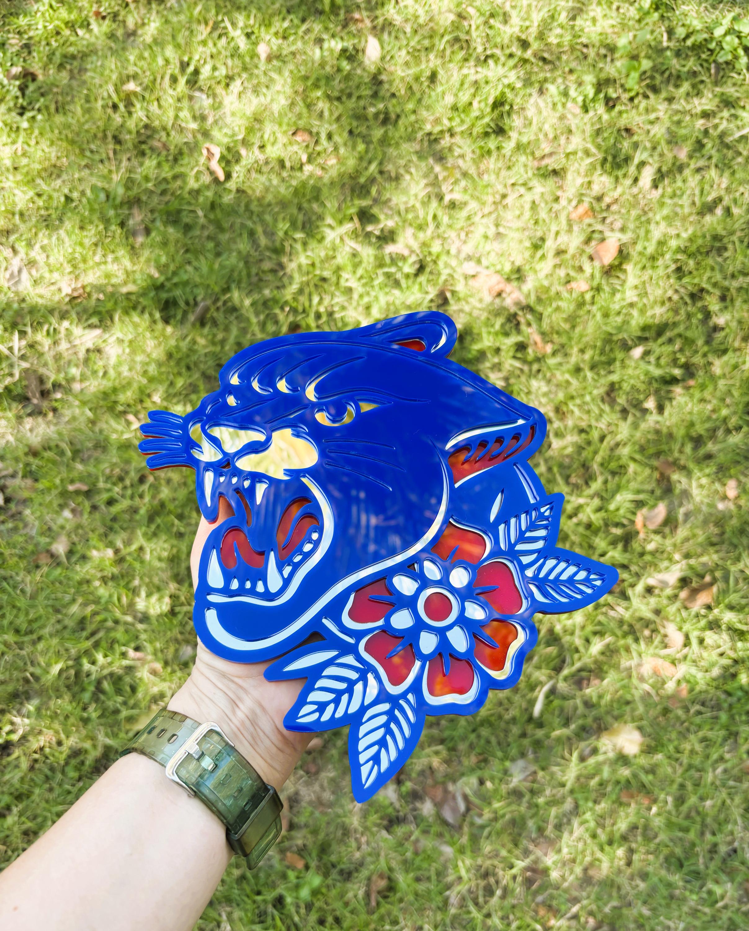 Blue panther design with floral elements held by a person against a grassy background