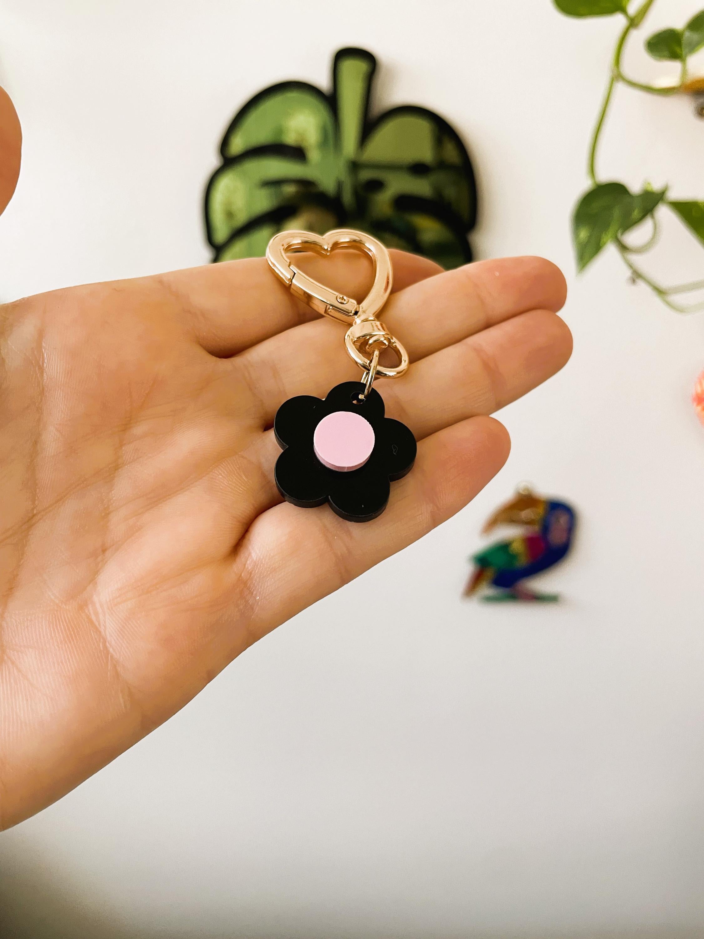 Hand holding a black flower-shaped keychain with a pink center against a light background.